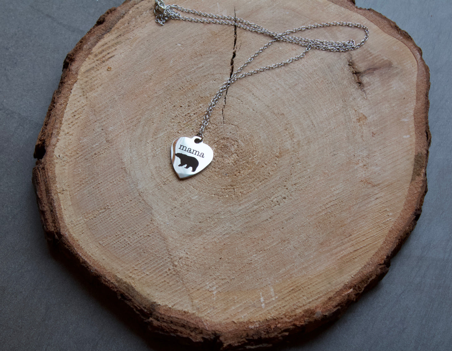 Stainless steel heart shaped necklace with "mama" and a bear embellishments done in black. Necklace is 18" long