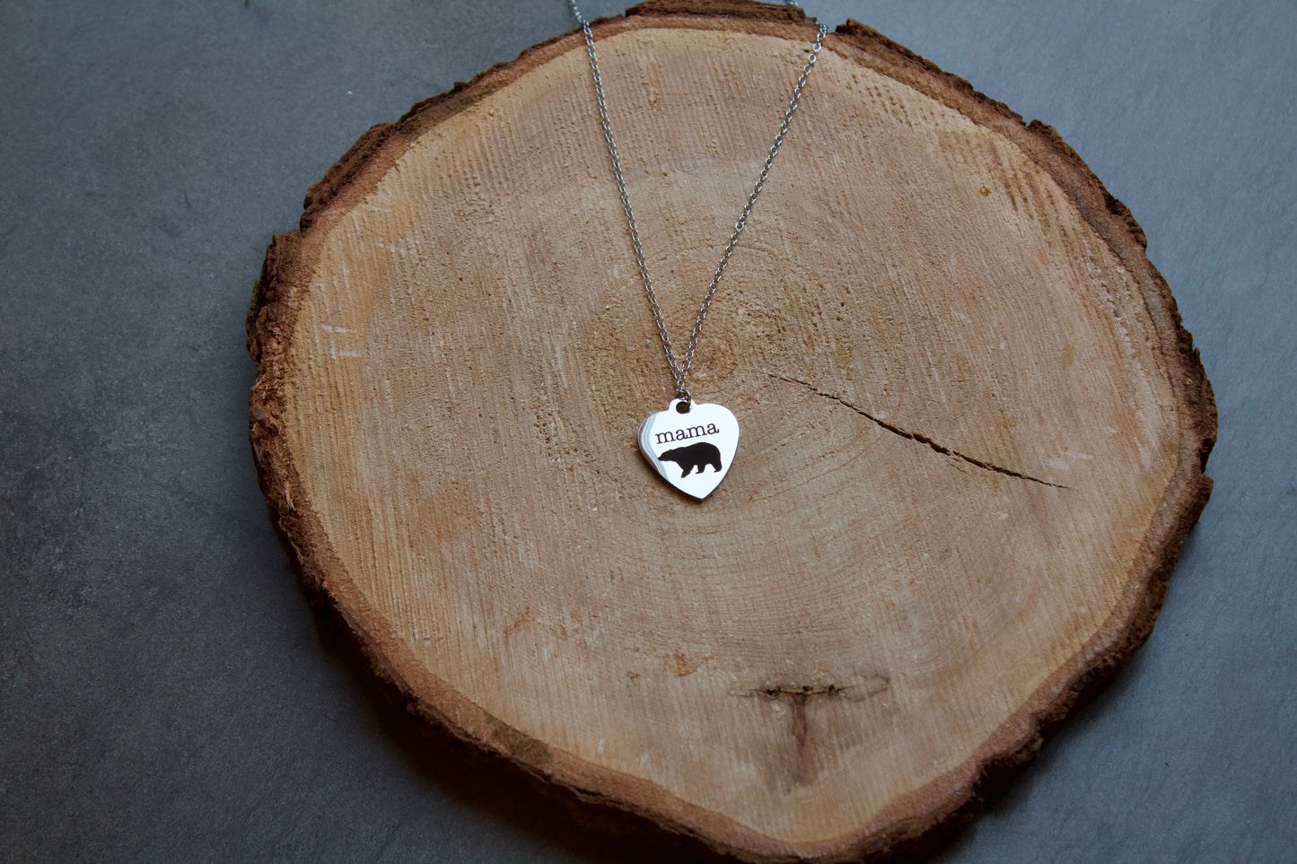 Stainless steel heart shaped necklace with "mama" and a bear embellishments done in black. Necklace is 18" long
