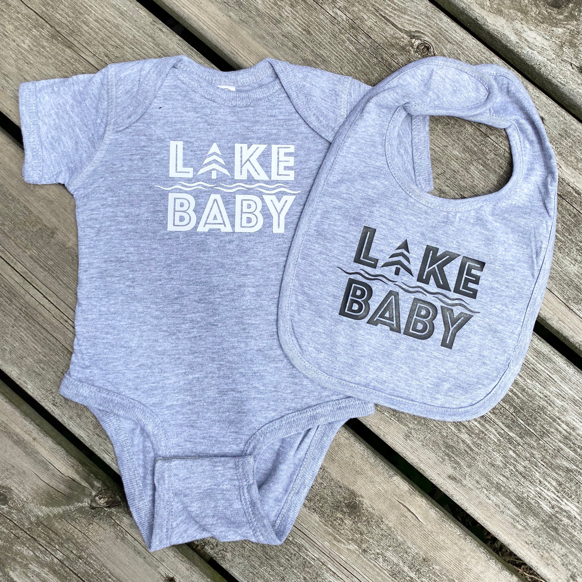 Heather grey cotton bib with black HTV logo that reads LAKE BABY. Heather grey cotton onesie with white HTV LAKE BABY logo.